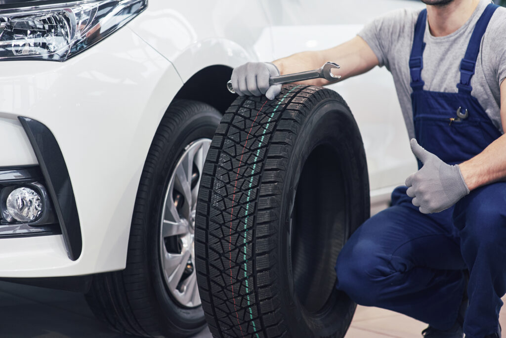 Technician with a blue workwear, holding a wrench and a tire while showing thumb up.